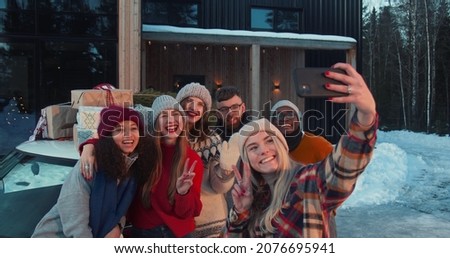 Group of happy multiethnic friends smile taking selfie pictures at snowy Christmas chalet house terrace slow motion.