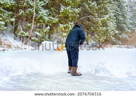 A man cleaning snow with a shovel. Clearing a skating or ice rink in the forest. Winter, fun, work, shoveling snow