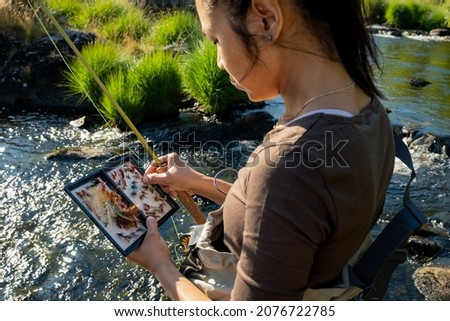 A close up of an asian female selecting fly fishing flies from a box Royalty-Free Stock Photo #2076722785