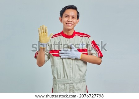 Portrait of handsome man wearing mechanical uniform swearing with hands on chest and open palms on gray background