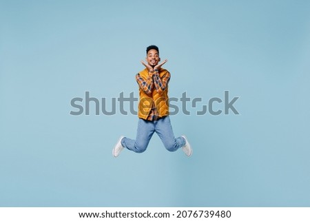 Full size body length stunning delight fascinating young black man 20s years old wears yellow waistcoat shirt jump raised hand to face isolated on plain pastel light blue background studio portrait