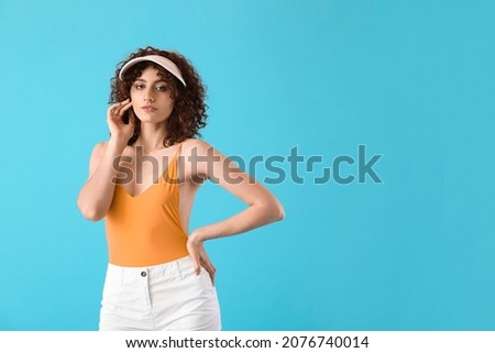 Young woman with hand near face wearing visor cap on blue background