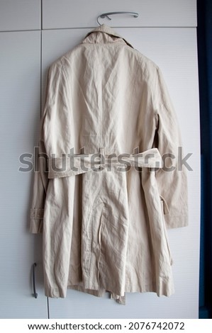 female coat with belt hangs on a hanger. Royalty-Free Stock Photo #2076742072