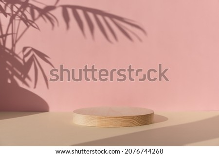 Premium podium with a shadow of tropical palm leaves on a pink wall. A cylindrical wooden scene on a beige table. Minimal abstract background for the presentation of a cosmetic product.