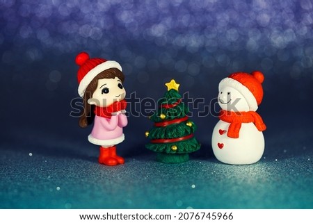 Small table figurines of a girl, a snowman and a Christmas tree on a shiny paper background. New Year photo postcard