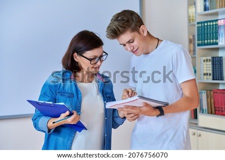 College student guy talking with female teacher in the library. Royalty-Free Stock Photo #2076756070