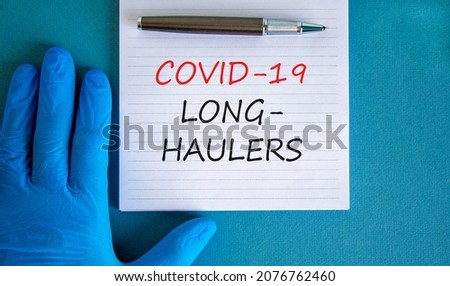COVID-19 long-haulers covid symptoms symbol. White card with words Covid-19 long-haulers. Doctor hand, pen, blue background, copy space. Medical, COVID-19 long-haulers covid symptoms concept.