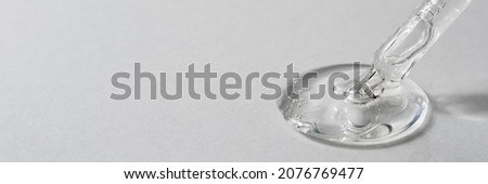 Drop of facial serum with bubbles pouring from transparent pipette on grey background. Web banner for cosmetic product advertising. Liquid gel with collagen closeup. Copy space, front view Royalty-Free Stock Photo #2076769477