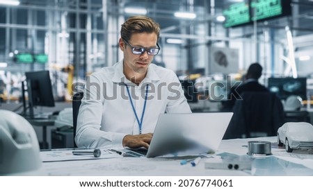 Young Handsome Engineer Working and Managing Projects on Laptop Computer in an Office at Car Assembly Plant. Industrial Specialist Working on Vehicle Parts in Technological Development Facility. Royalty-Free Stock Photo #2076774061