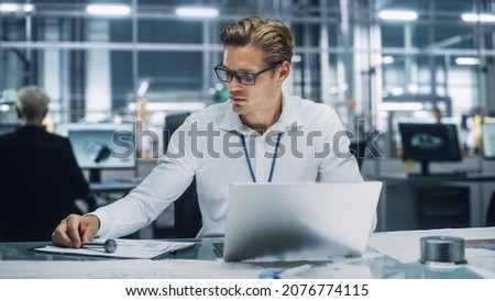 Young Handsome Engineer Working and Managing Projects on Laptop Computer in an Office at Car Assembly Plant. Industrial Specialist Working on Vehicle Parts in Technological Development Facility. Royalty-Free Stock Photo #2076774115