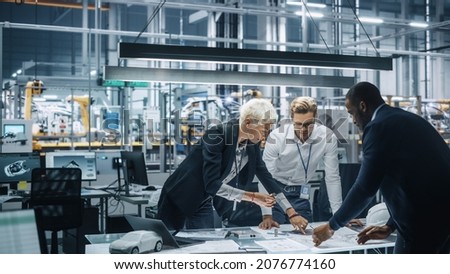 Young Diverse Team of Automotive Engineers Working in Office at Car Factory. Industrial Designer Talks About Electric Engine Parts with Colleagues, Discussing Different Technological Applications. Royalty-Free Stock Photo #2076774160