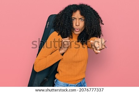 Young african american girl wearing guitar case pointing with finger to the camera and to you, confident gesture looking serious 