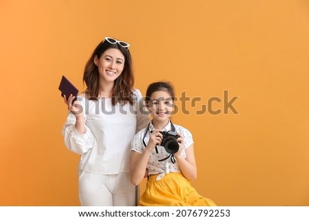 Happy mother and daughter with photo camera and passports on color background. Concept of tourism