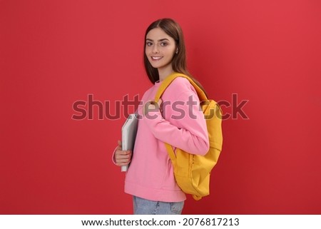 Teenage student with backpack and book on red background
