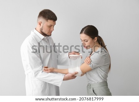 Doctor applying bandage onto arm of young woman on light background