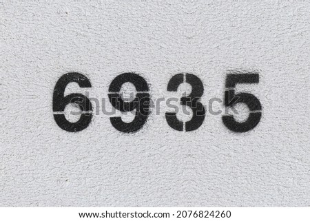 Black Number 6935 on the white wall. Spray paint. Number six thousand nine hundred thirty five.