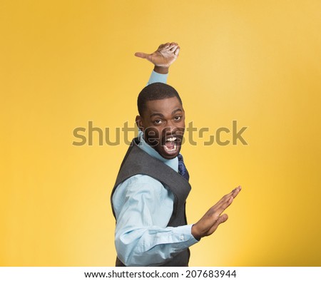 Closeup portrait angry mad furious, company man raising hands in air attack with karate chop isolated yellow background. Negative human emotion facial expression feeling, body language, signs, symbols
