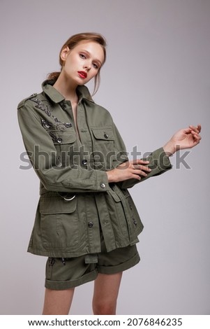 High fashion photo of a beautiful elegant young woman in a pretty green patterned jacket, short shorts posing over white, soft gray background. Slim figure. Studio Shot.