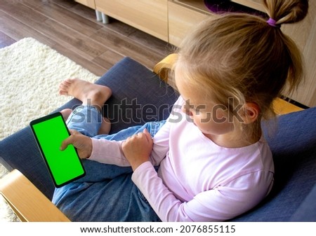 selective focus on the hands of a child at home sitting in a chair using a smartphone with a green screen. Using a mobile phone, browsing the Internet, content, videos, blogs, playing games