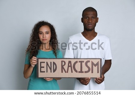 African American woman and man holding sign with phrase End Racism on grey background