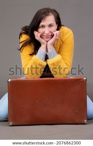 Happy fifty year old woman in yellow clothes with vintage suitcase on gray background. Portrait of a middle-aged woman.
