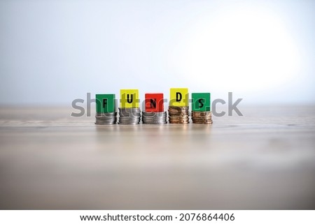 Wooden blocks with FUNDS text on top of stacked coins. Noise is visible due to the texture of the subjects