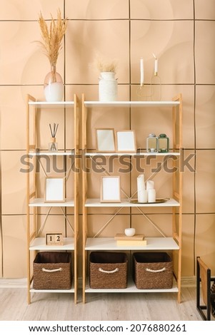 Shelf unit with blank photo frames and decor near color wall in room