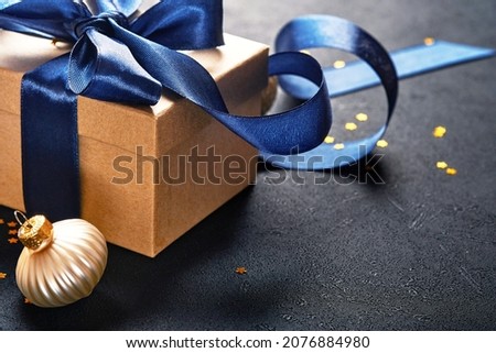 Holiday gift box or present with blue ribbon, golden confetti and gold baubles on black background. Magic christmas greeting card. Christmas Decoration. Border design. Mock up. Top view.