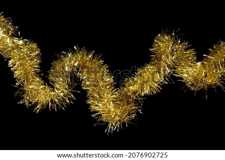 Golden tinsel decorative garland on black background Royalty-Free Stock Photo #2076902725