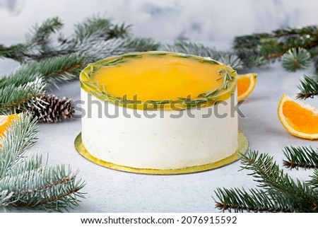 Christmas oange mousse cake decorated with rosemary on a white background with a Christmas tree.  Sweet Christmas or winter holidays pastry food concept. 