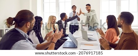 Mixed race business team celebrating good results in office meeting. Happy young black man gives high five to coworker while diverse multi ethnic teammates are applauding. Teamwork and success concept Royalty-Free Stock Photo #2076917185