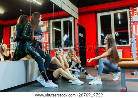 Four tired, happy athletic girls chat and relax after a hard workout in the gym