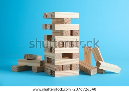 Jenga tower made of wooden blocks on light blue background Royalty-Free Stock Photo #2076926548