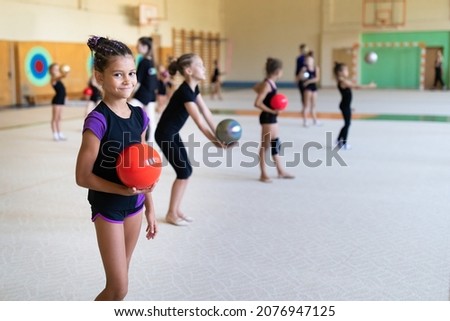 Girl gymnast doing exercise with ball on training in gym with other girls