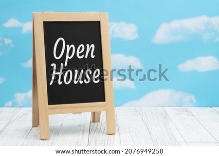 Open House sign on standing chalkboard on weathered wood with clear sky