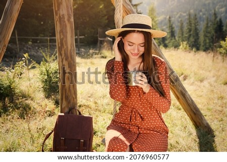 Young woman with hot drink resting outdoors on sunny day