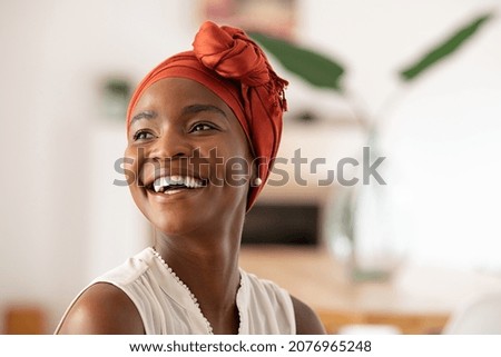 Beautiful mature black woman with african turban relaxing at home. Cheerful middle aged black woman in casual clothing with traditional headscarf at home laughing. African american lady smiling. Royalty-Free Stock Photo #2076965248
