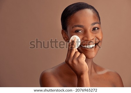 Happy smiling beautiful african woman cleaning skin by cotton swab. Portrait of mature woman using cotton pad against brown background to clean her face. Portrait of beauty lady removing make up. Royalty-Free Stock Photo #2076965272