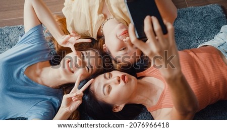 Above view close up group of Asia ladies with happiness enjoy moment hold smartphone smiling take memories picture lying on carpet in floor living room at home. Lifestyle activity quarantine concept. Royalty-Free Stock Photo #2076966418