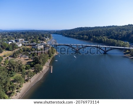 Aerial view. A large blue river and a bridge connecting the two banks. Small green city, mountains, blue cloudless sky. Beautiful landscape. Advertising of tourist destinations, ecology. Royalty-Free Stock Photo #2076973114