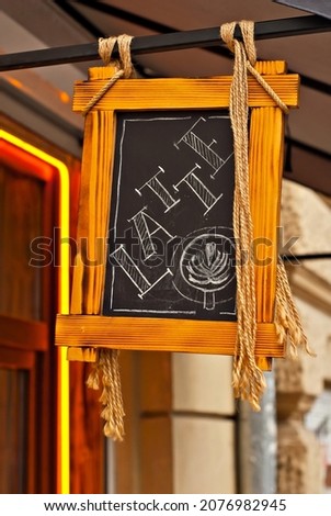 Wooden sign with black space for text. A wooden frame hangs near a restaurant on the street. Mockup for design. The word Latte is written in chalk on a black background.