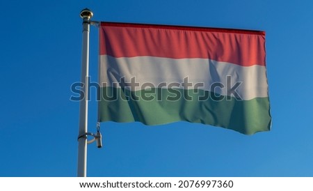 National flag of Hungarian on a flagpole in front of blue sky with sun rays and lens flare. Diplomacy concept. International relations. Space for text.