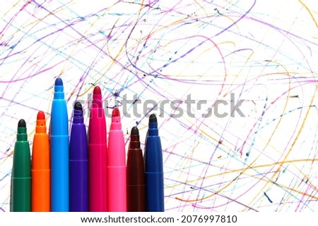 Bright colorful multicolored felt-tip pens lie on white paper with drawn doodles.