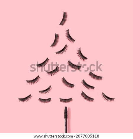 Christmas tree silhouette made of eyelashes and mascara brush on bright pink background. Creative New Year concept. Minimal beauty makeup layout.