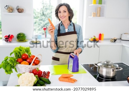 Photo of age cheerful lady cut carrot wear apron jeans shirt at kitchen alone
