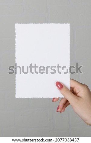 Woman hands holding blank paper sheet A5 size or letter on grey wall background. Close up of 5x7 ratio card white empty card mockup in female hand, invitation or greeting card