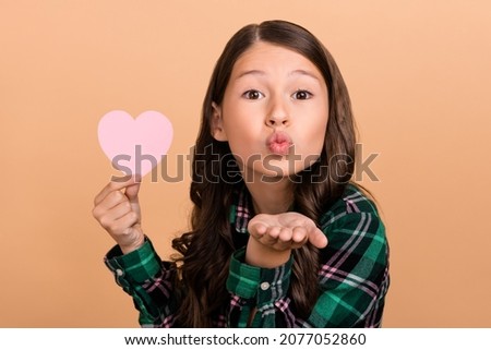 Photo of excited flirty school girl dressed checkered clothes holding pink heart sending arm kiss isolated beige color background