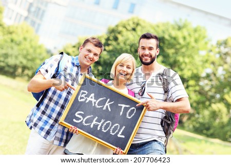 A picture of a group of students standing in the park and holding a blackboard
