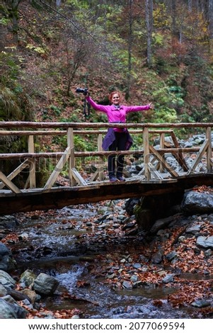 Woman travel photographer with camera on a bridge over river in a vibrant autumn scene in the mountains