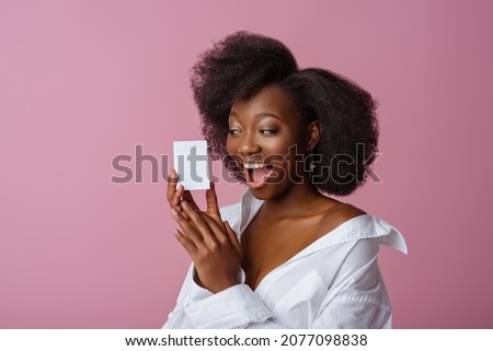 Yong beautiful happy smiling surprised African American woman, model wearing elegant jewelry, classic shirt, holding small white box, posing in studio, on pink background. Copy, empty space for text Royalty-Free Stock Photo #2077098838